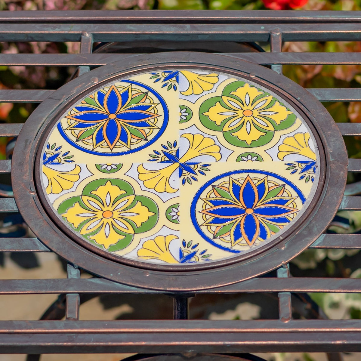 Round tabletop inset with blue, yellow, and green floral mosaic tiles, framed by dark metal slats.
