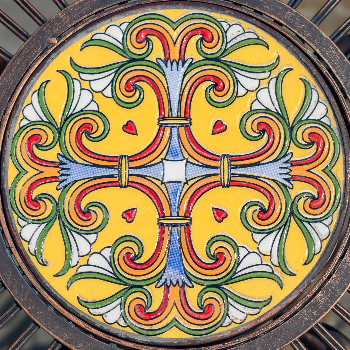 Close-up of a round yellow mosaic tile with a colorful, symmetrical floral scroll pattern.