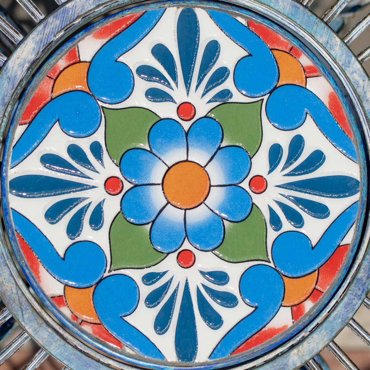 Close-up of a round mosaic with a central flower and blue, green, orange, red, and white patterns.