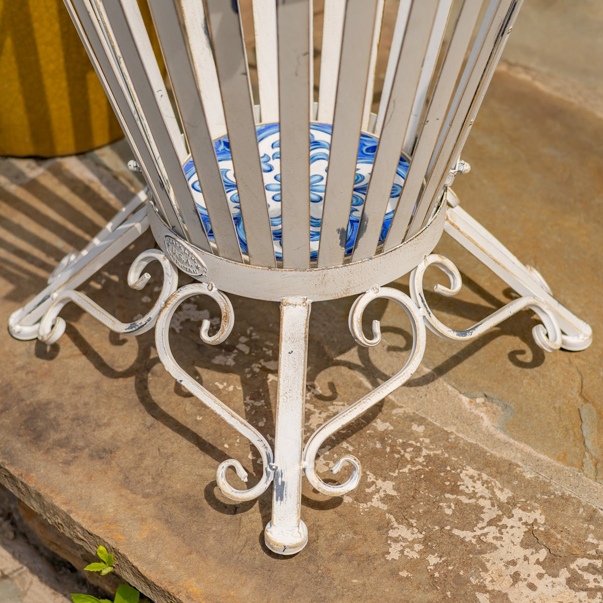 Close-up of the holder’s curved antique-white feet and scrollwork against a stone patio.