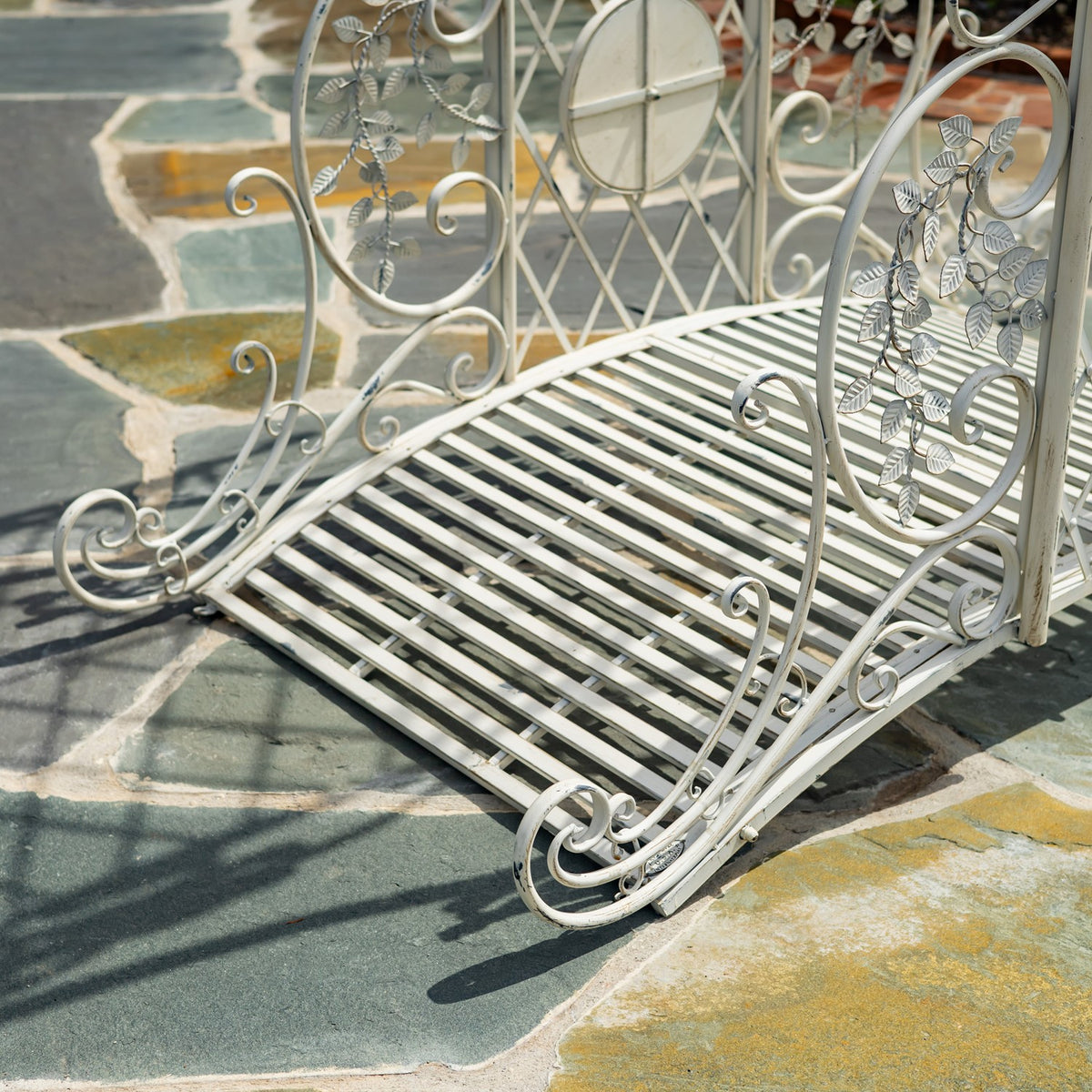 Angled view of the bridge’s slatted metal deck and curled side rails on a stone patio.