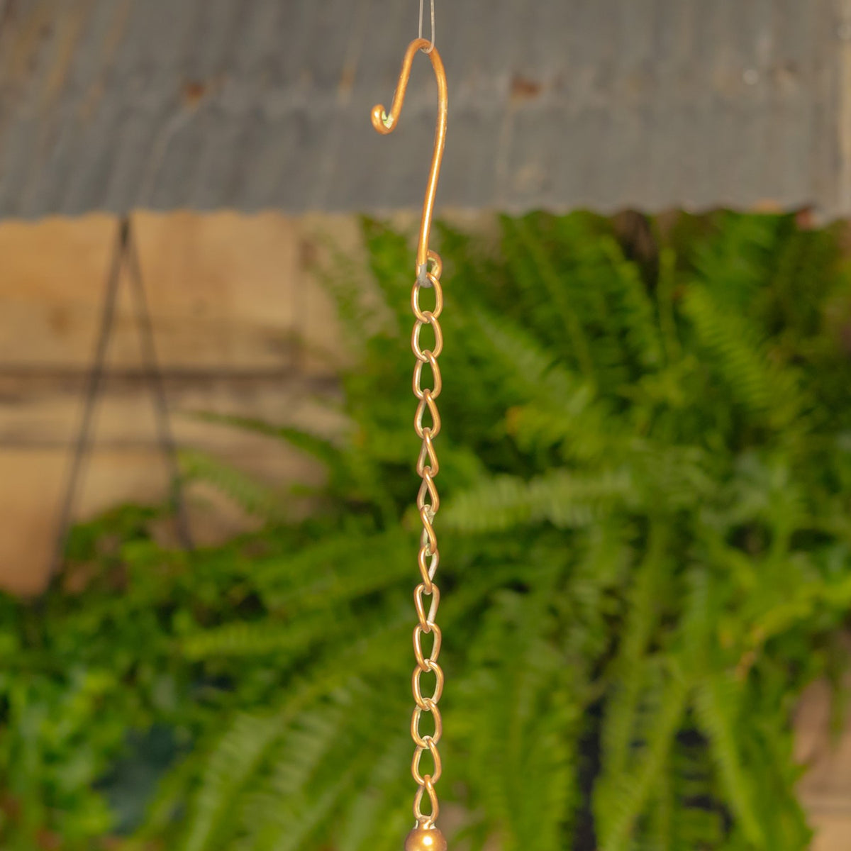 Close-up of the gold-toned hanging chain and curved hook against a wooden garden backdrop.
