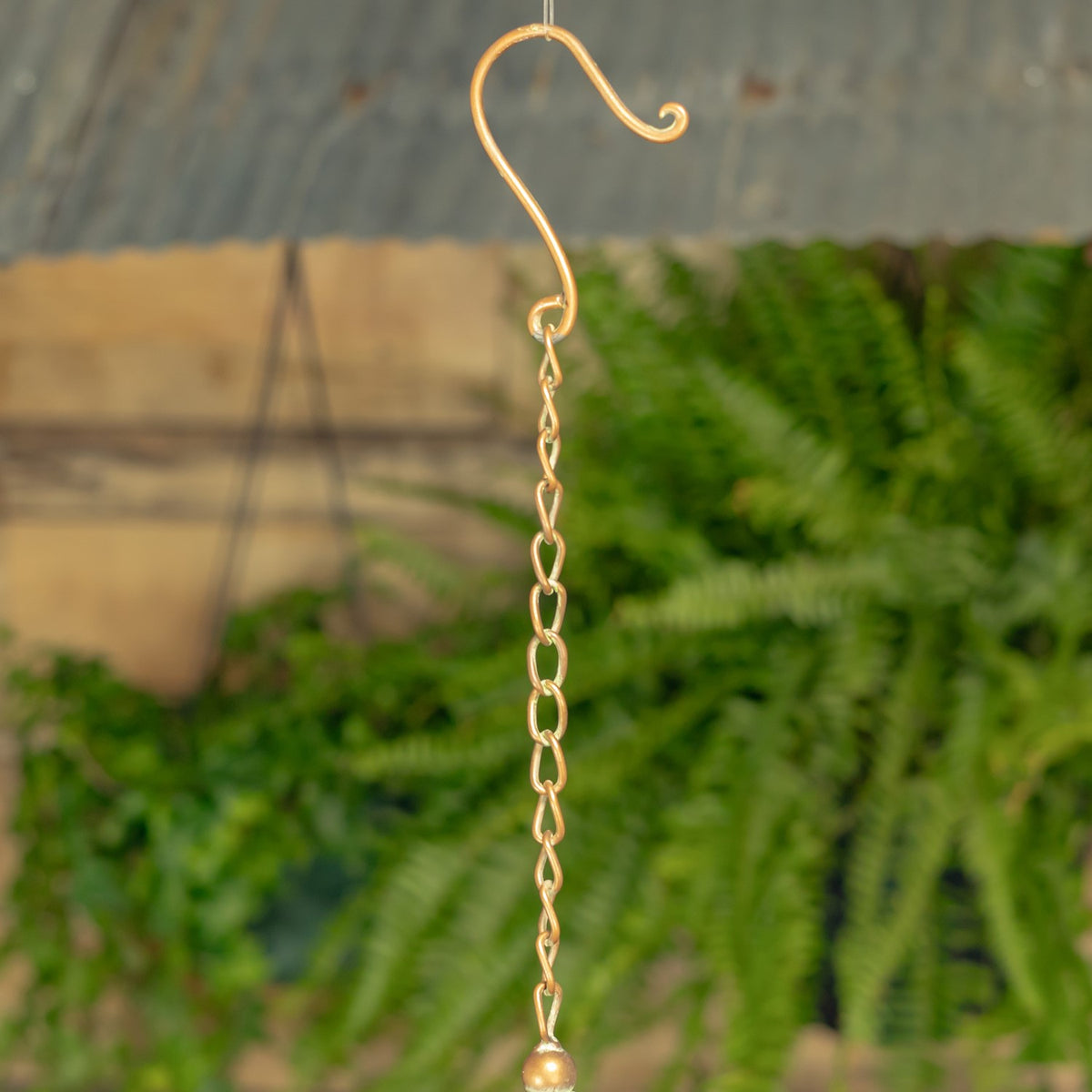 Curled metal hanging hook connected to a short chain against a softly blurred background.