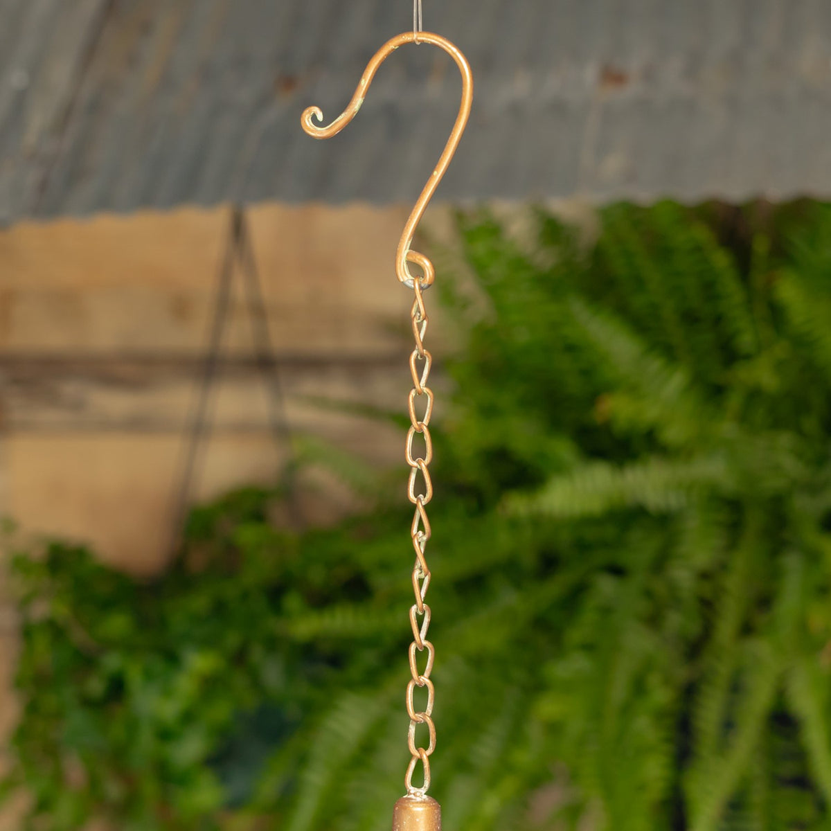 Curved metal hook and linked chain shown against a blurred garden backdrop.