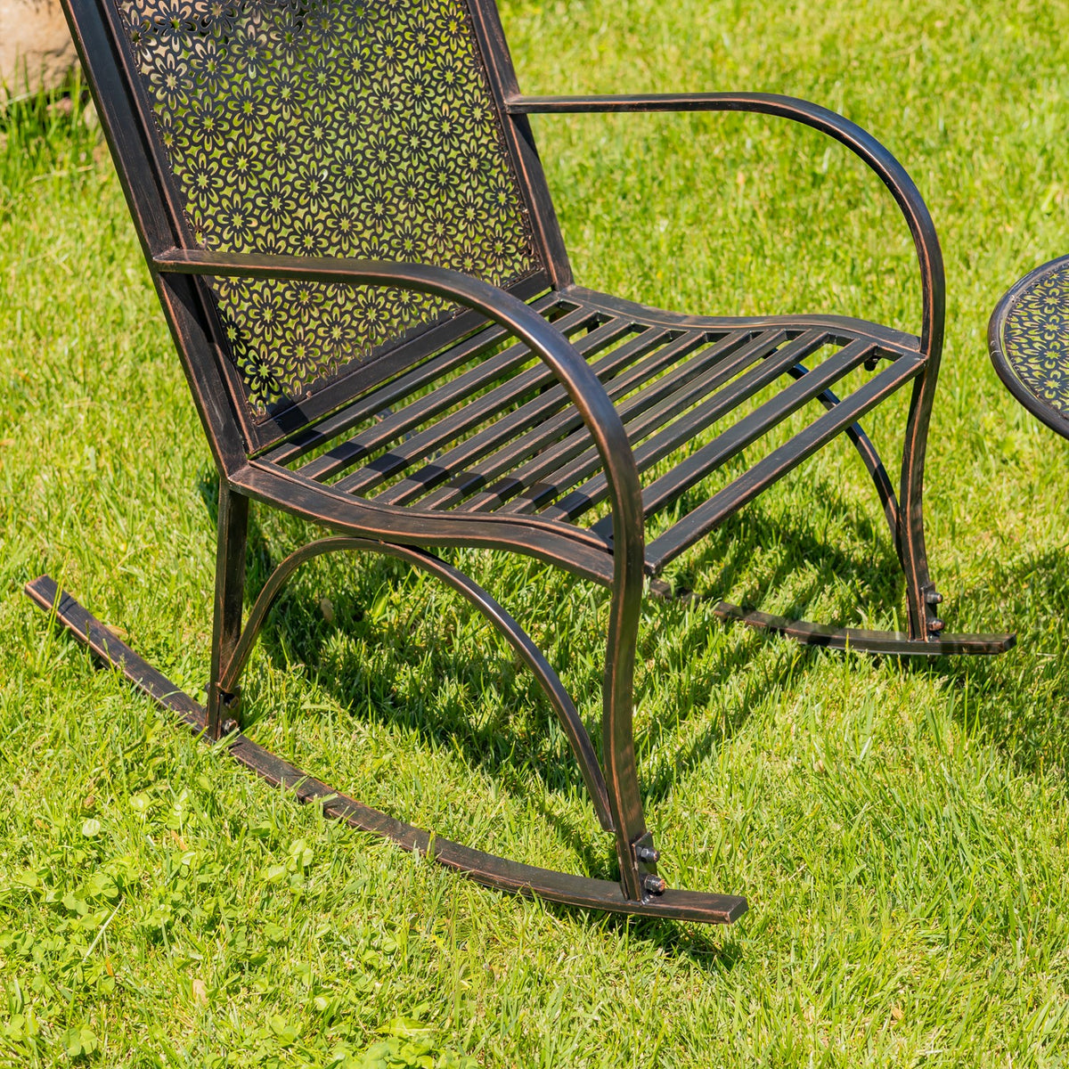Close view of a metal rocking chair with curved arms, slatted seat, and floral-patterned back.