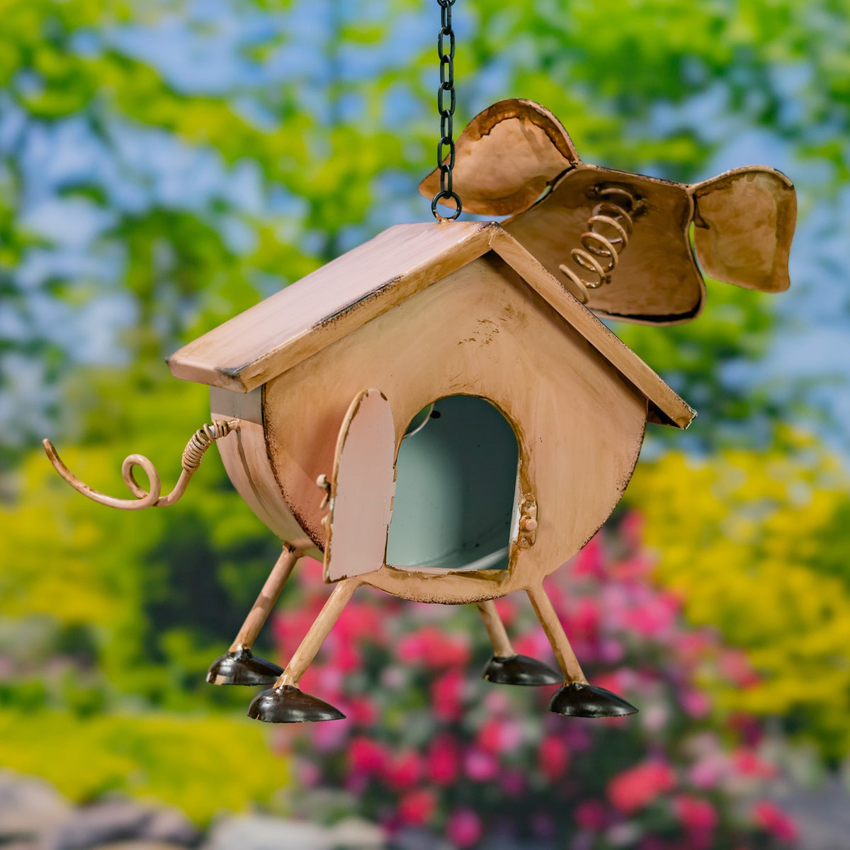 A metal birdhouse shaped like a cow, shown from the side with an open doorway and hanging chain.