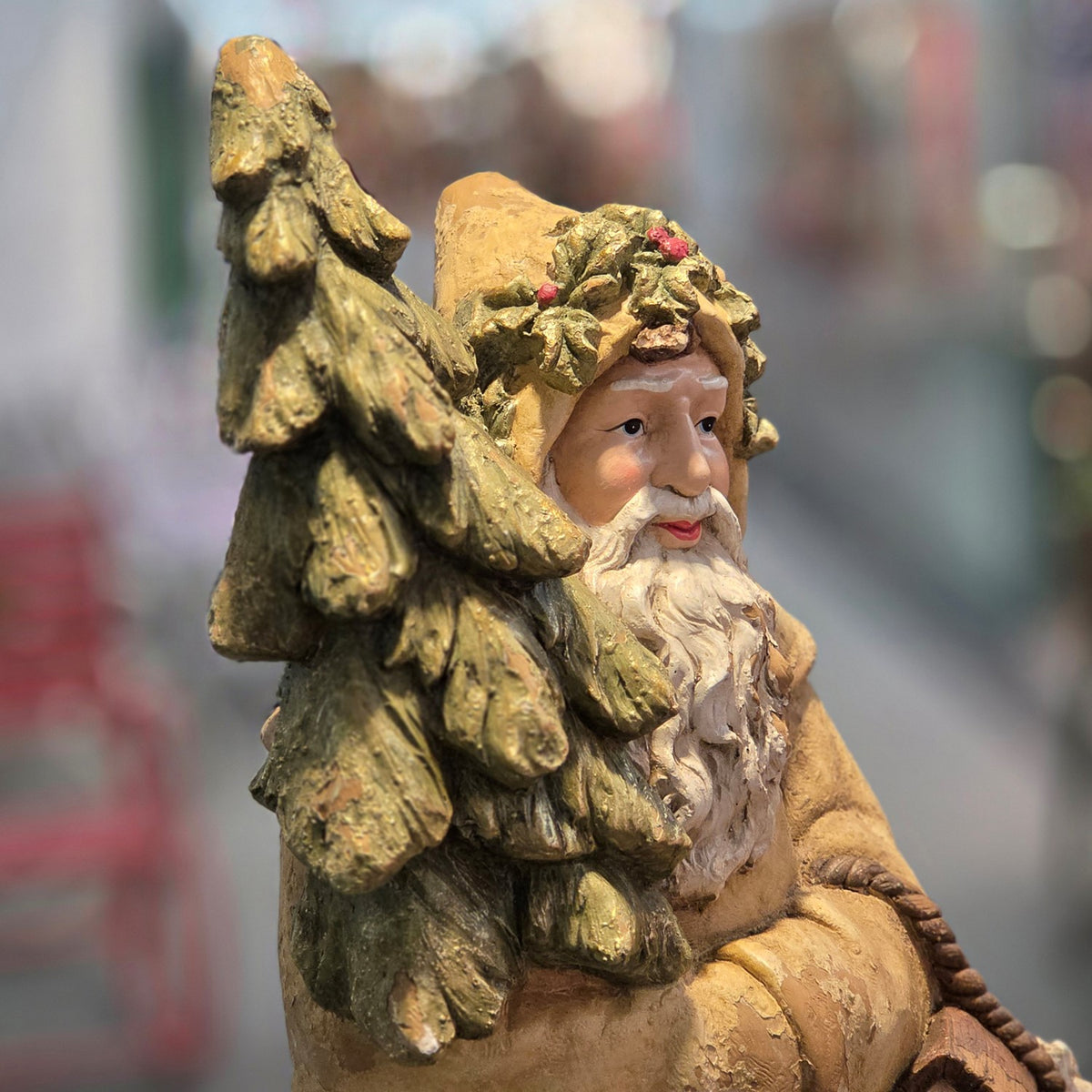 Close view of Santa’s face and textured evergreen tree, with a leafy wreath around his hat.