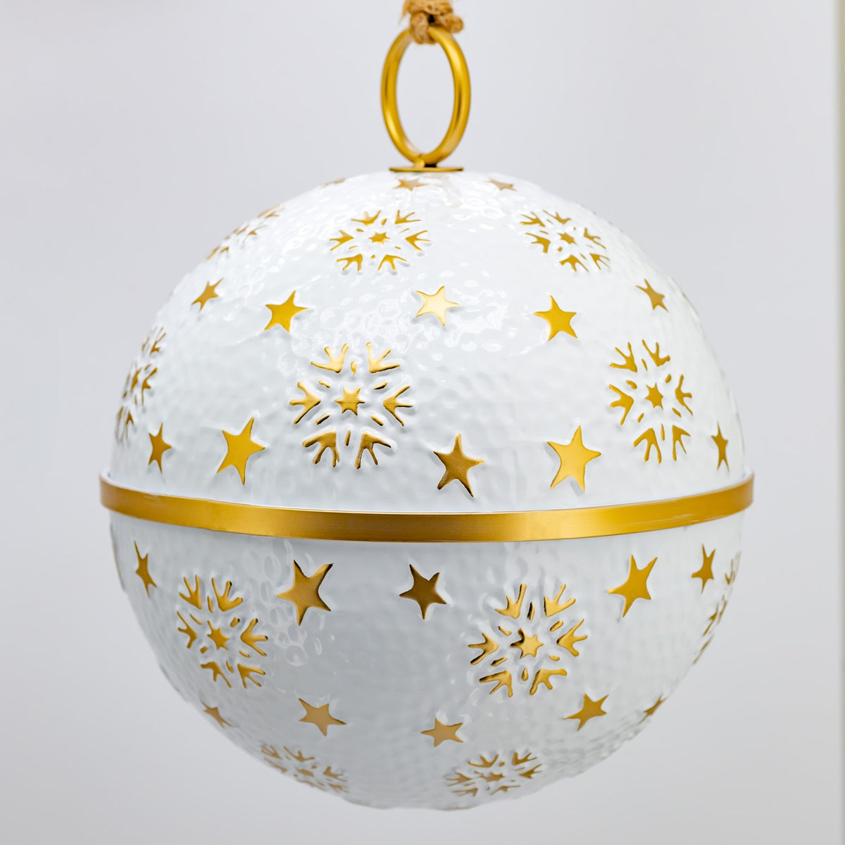 Close view of a white bauble with raised gold stars, snowflakes, and a gold band around its middle.