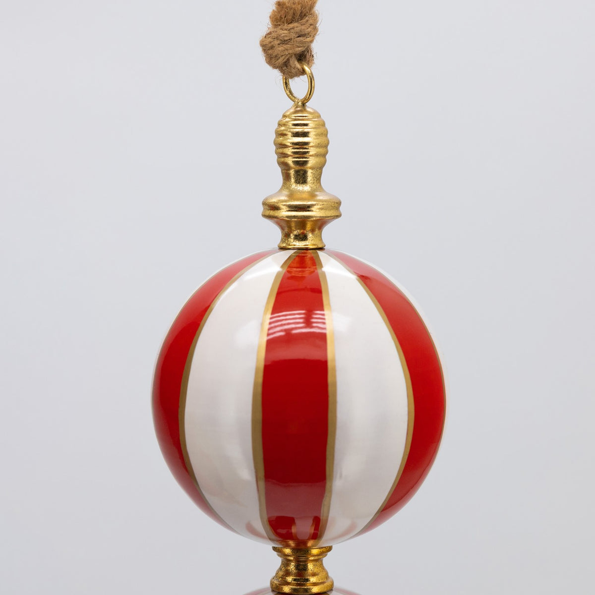 Close-up of a glossy red and white striped sphere with gold-colored trim and a hanging loop.