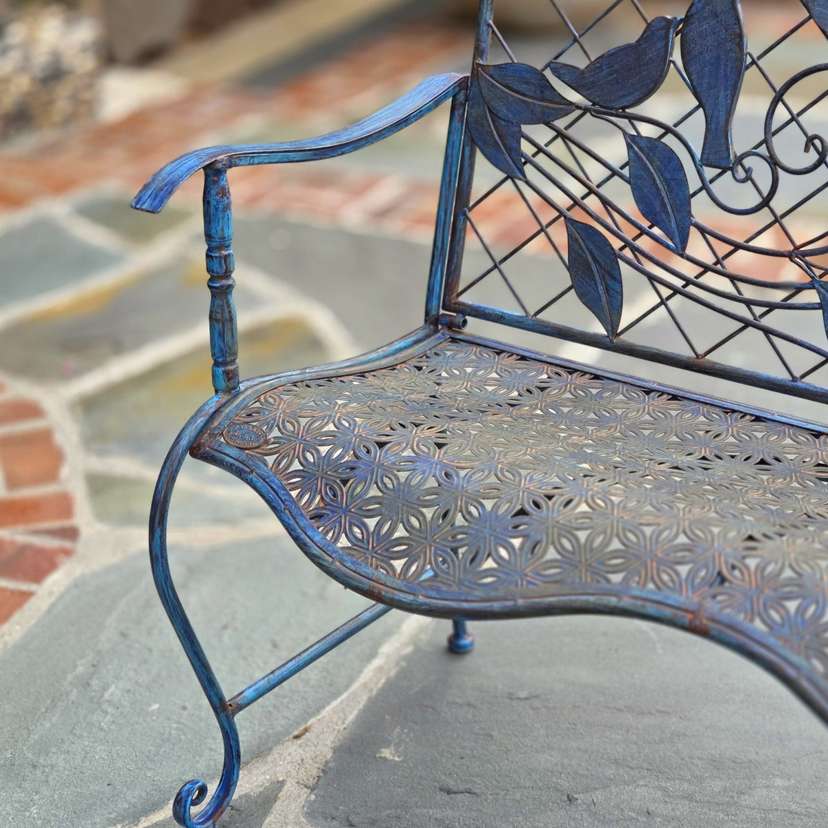 Close-up of the patterned metal seat, curved armrest and scroll-shaped front leg.