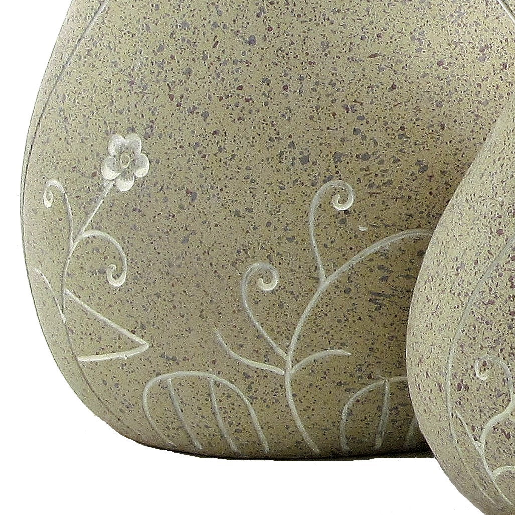 Close view of a pale flower and curling white stems etched across a speckled bird ornament.