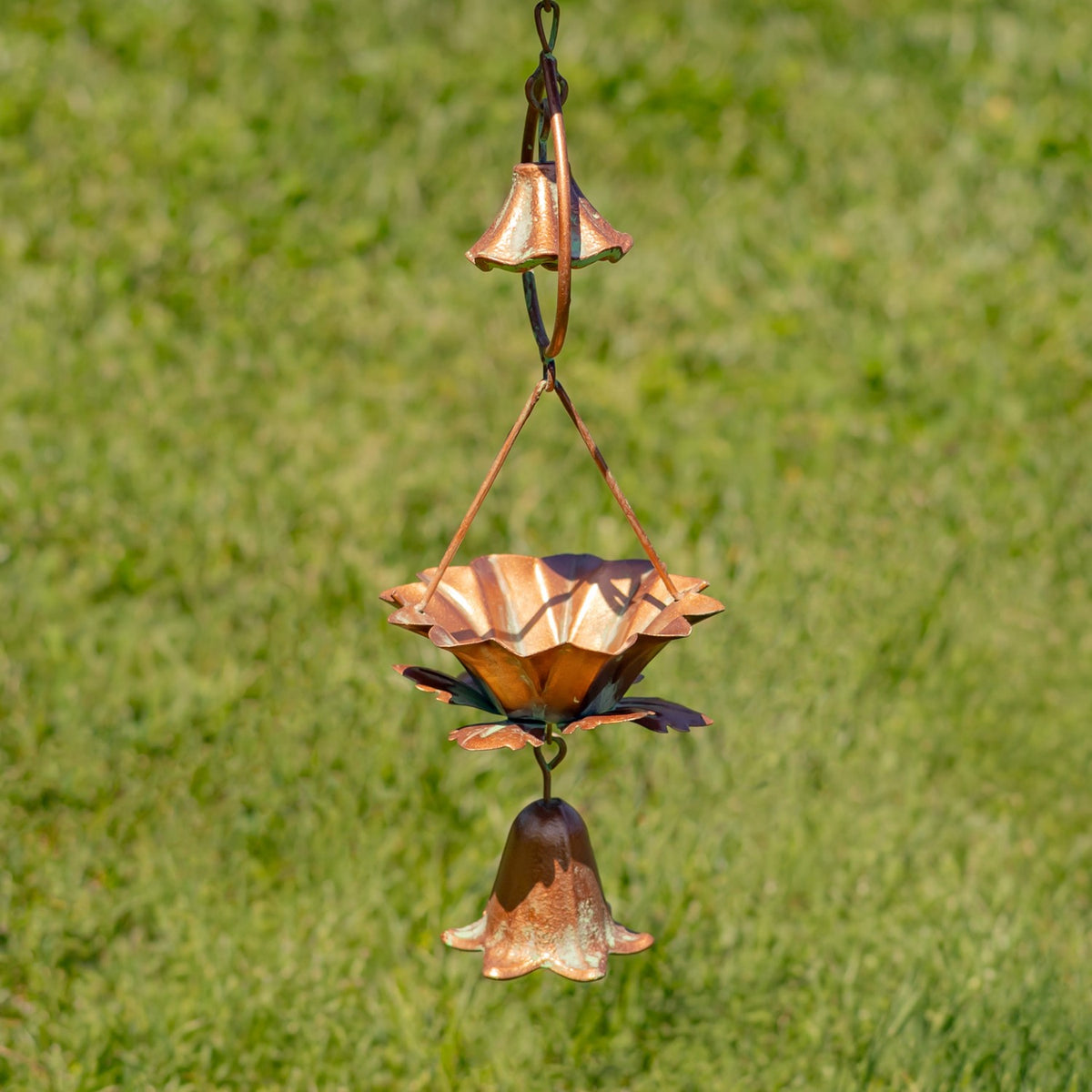 A lotus-shaped cup hangs between two bell-shaped pieces against a grassy background.