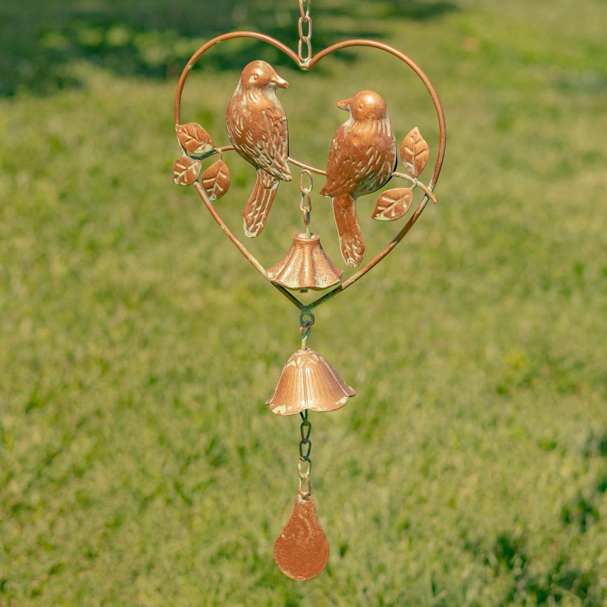 Close-up of two birds, leaves and bells within a copper-colored heart frame.