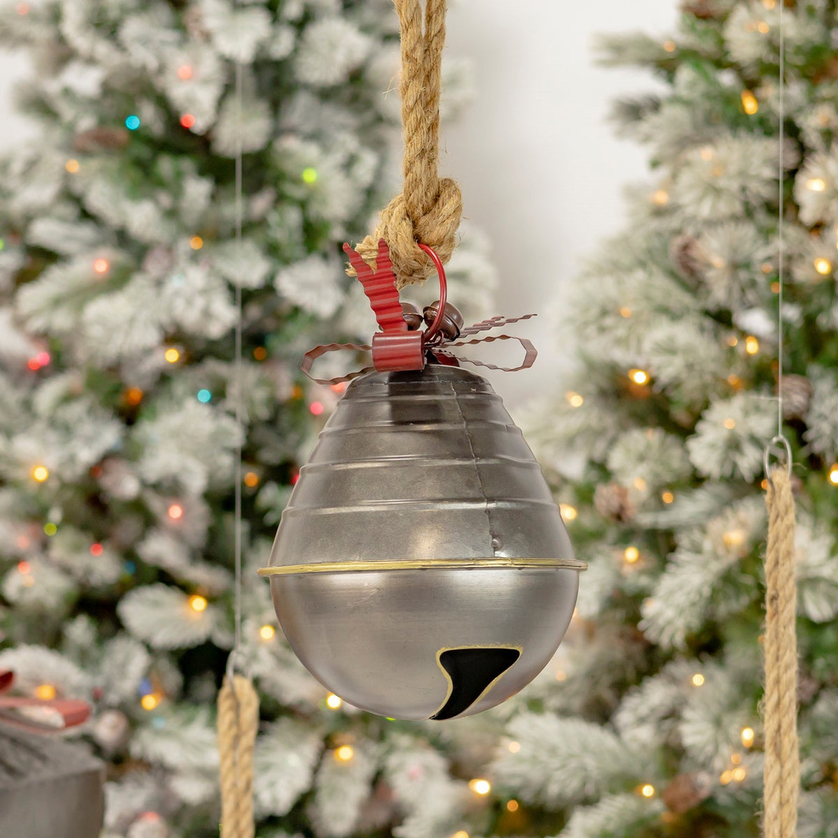 Tiered metal bell with a wide lower opening, red bow, and rope hanger against a Christmas tree.