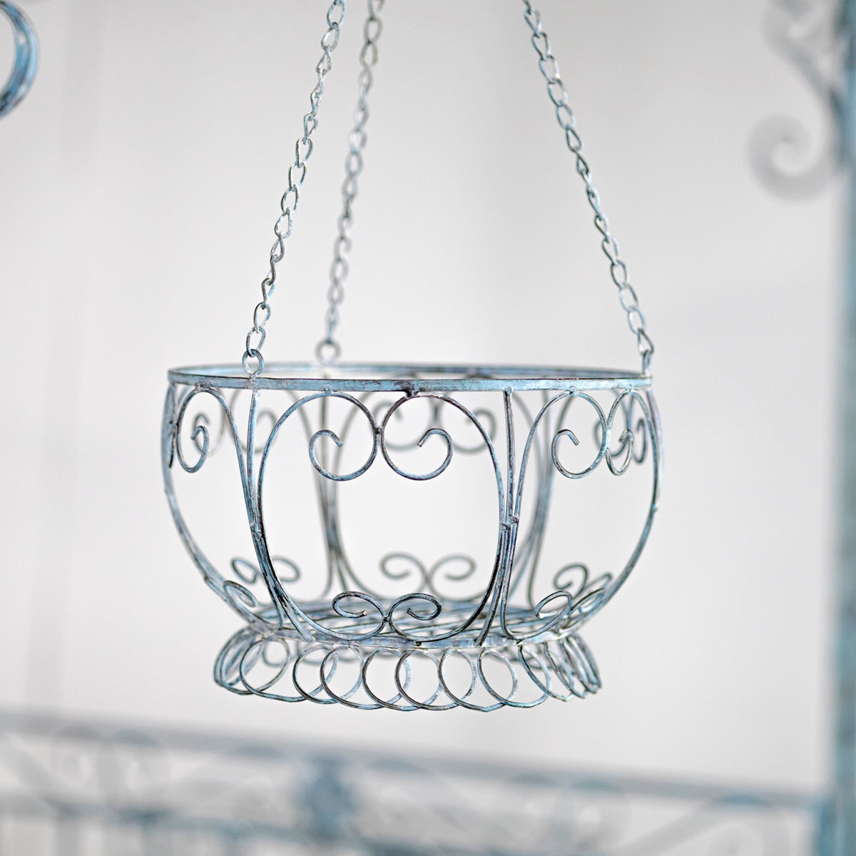An empty blue-gray wire planter with curled metalwork hangs from three chains.