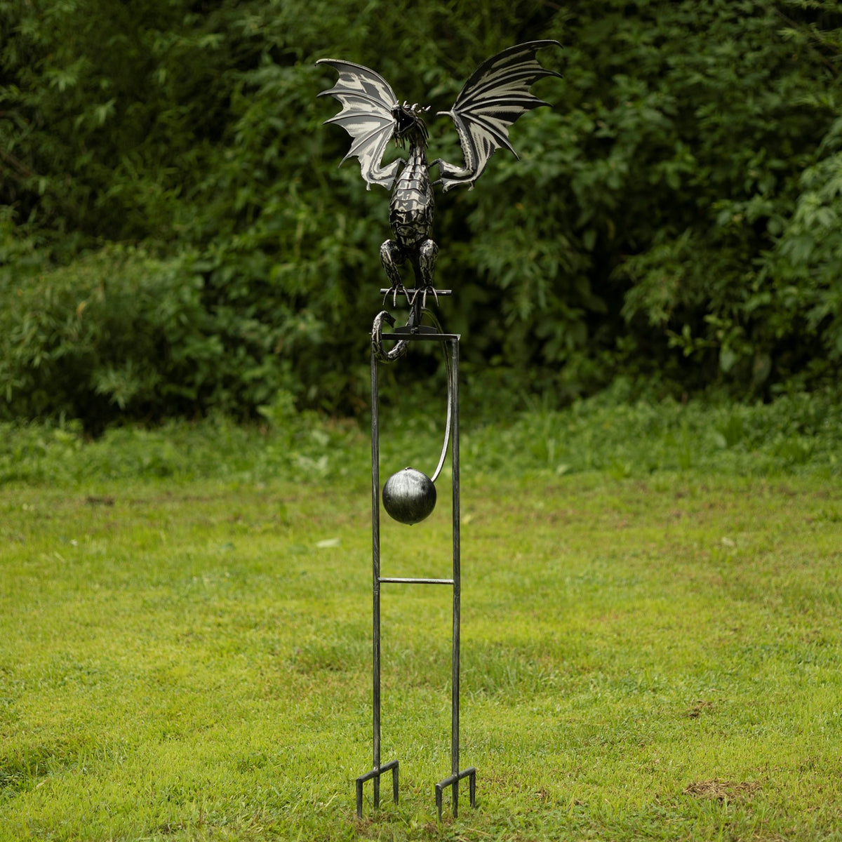 Full view of the dragon stake with its winged figure, hanging metal sphere, and forked ground anchors.
