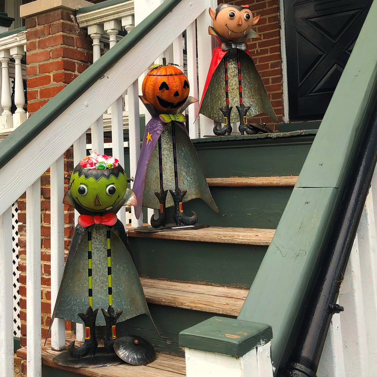 Pumpkin figurine stands on outdoor stairs between a green character below and another figure above.