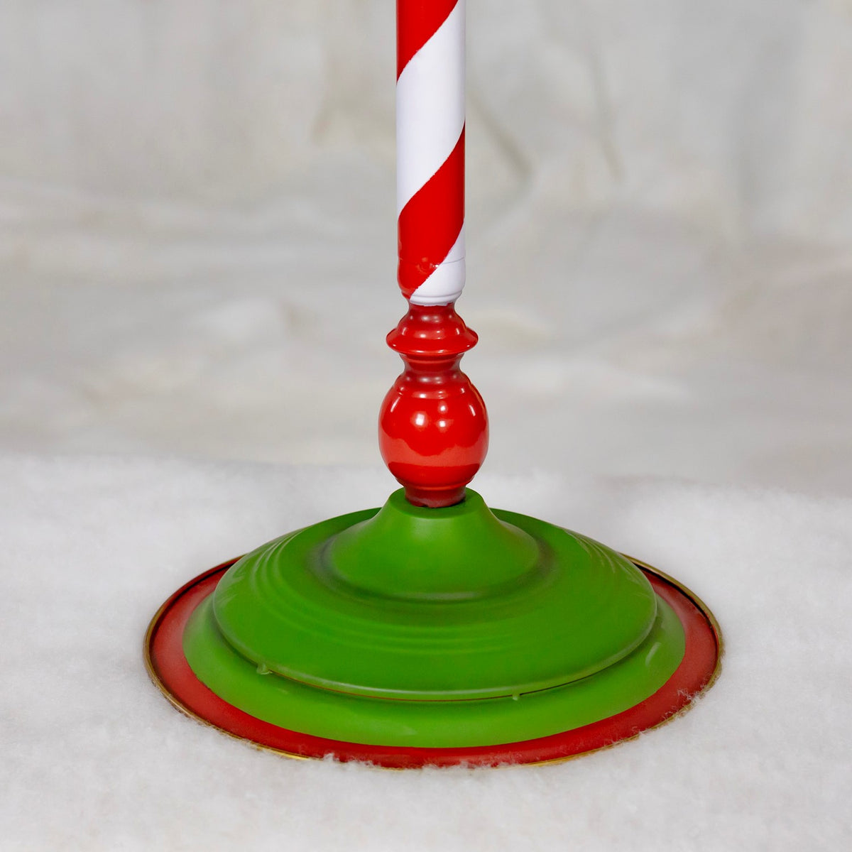 Green tiered circular stand base with a red rim resting on snow beneath the striped post.