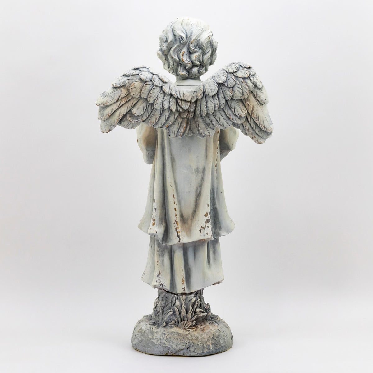 Rear view of a winged angel statue in a long robe, standing on a textured base.