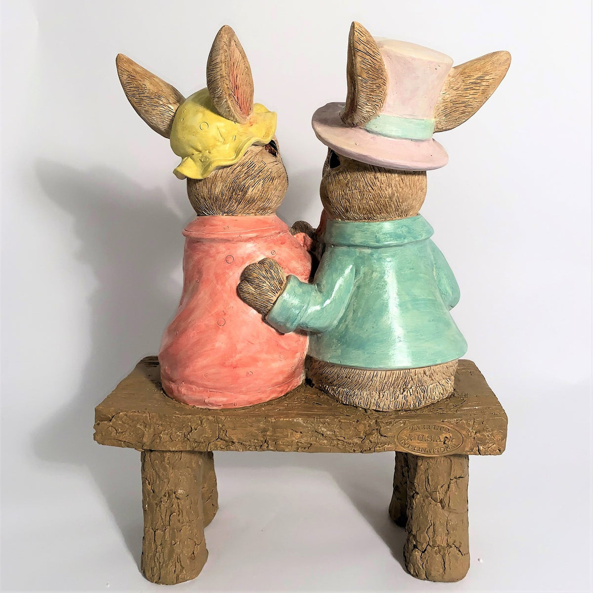 Rear view of the seated rabbits on the bench, with one rabbit's arm around the other.