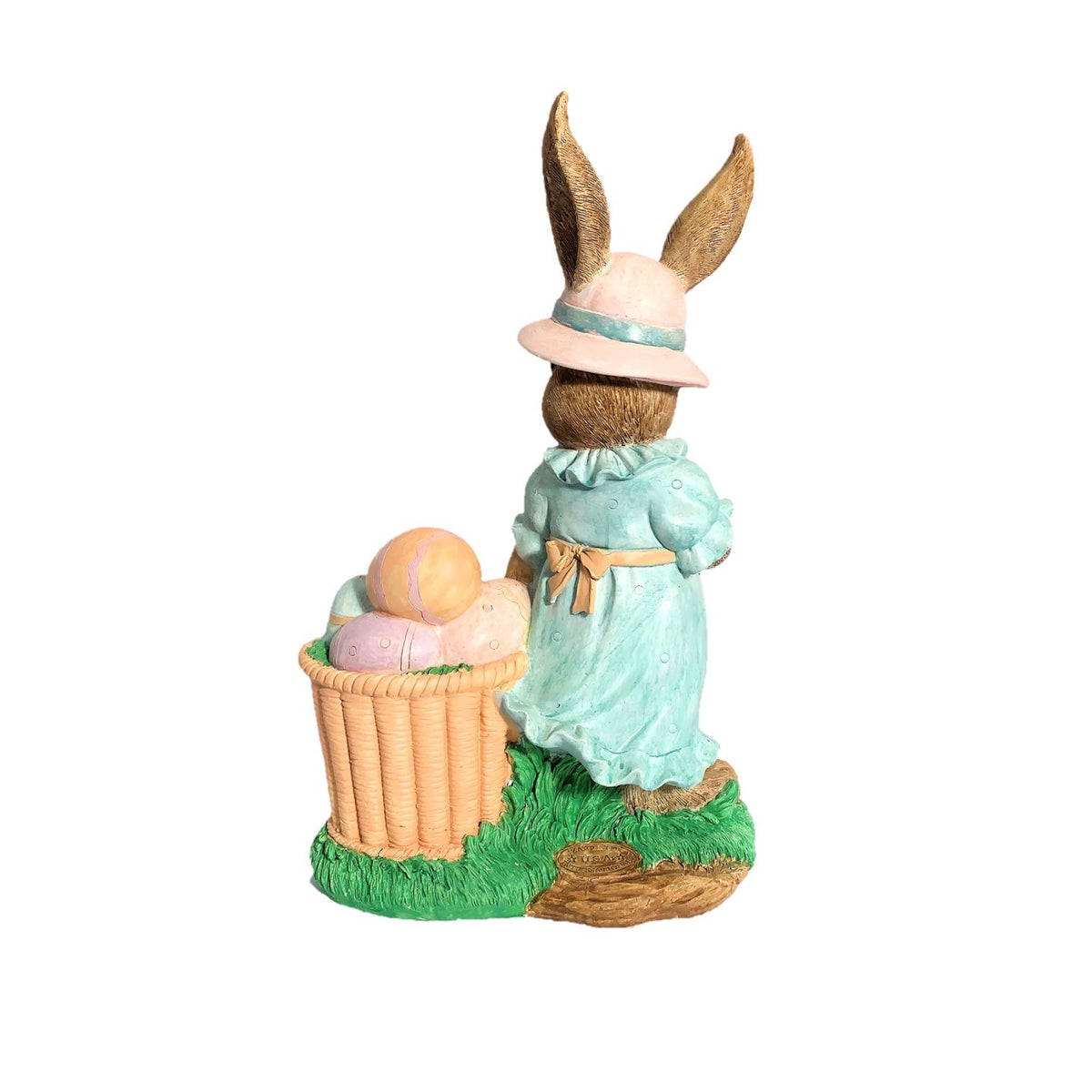 Rear of the rabbit statue showing its aqua dress and a basket of pastel eggs on the grassy base.