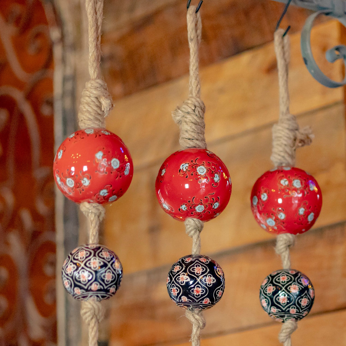 Three red floral balls and three dark ornamental balls hang in a close-up on separate cords.