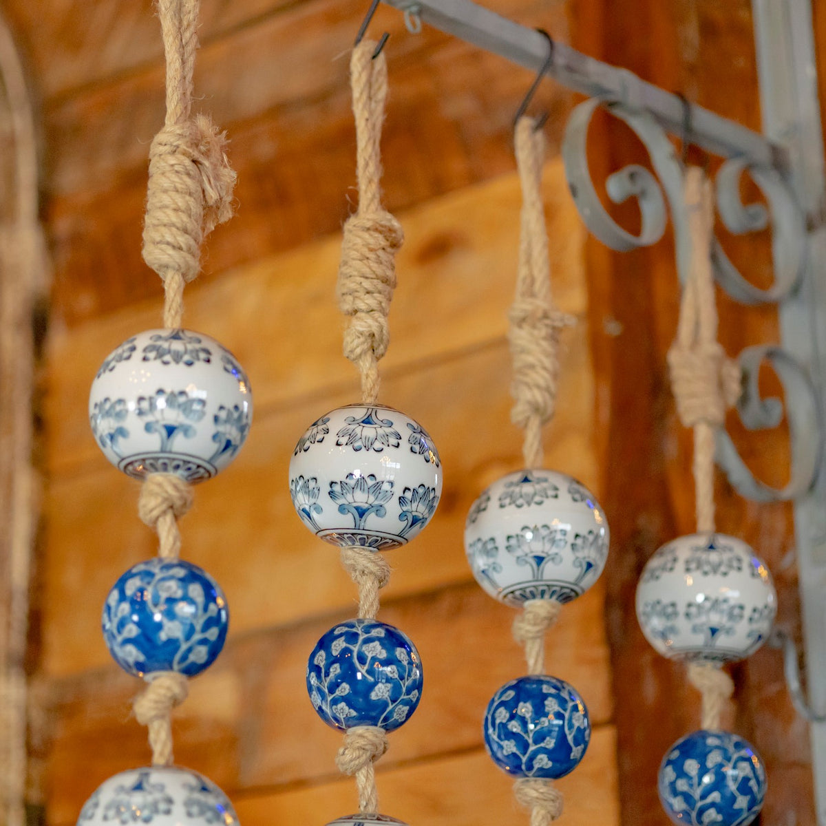 Rope loops suspend blue-and-white patterned ceramic balls from a decorative metal wall hook.