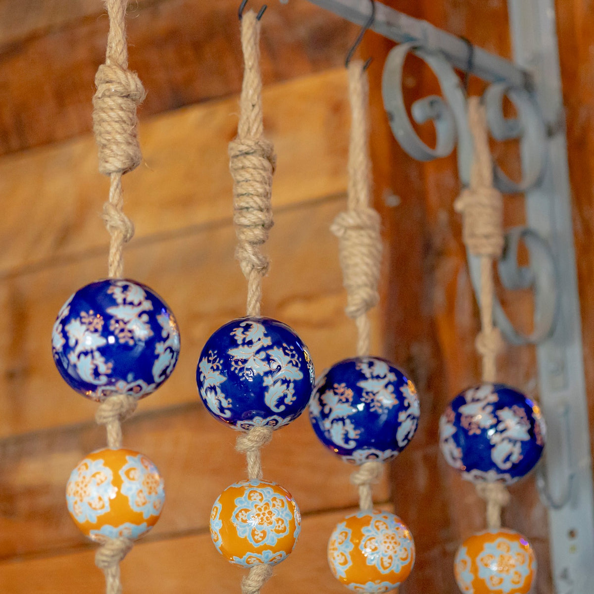 Four blue ceramic balls above orange ones hang from knotted cords beside a metal bracket.