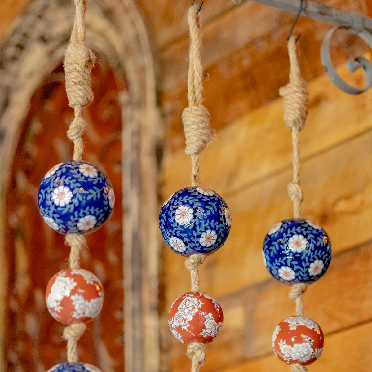 Three patterned porcelain balls hang from thick, wrapped twine against a wooden wall.