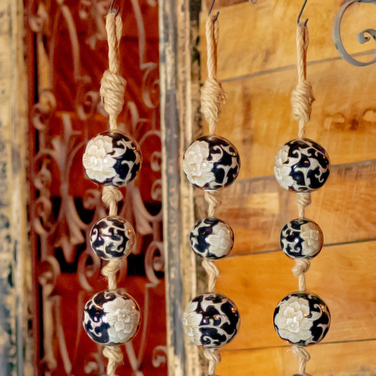 Three patterned ball strands hang from hooks against a warm wooden wall and decorative metalwork.