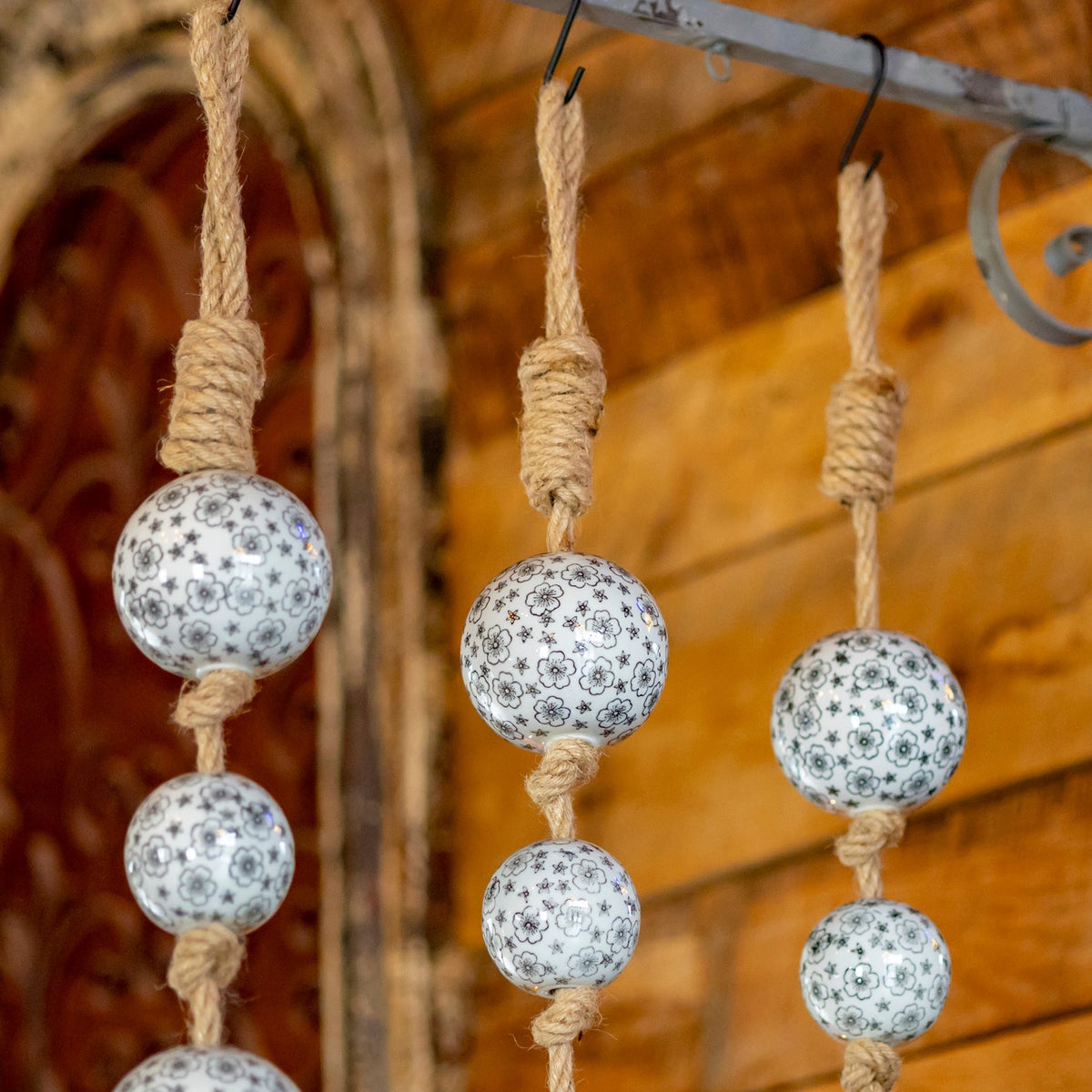 Patterned ceramic balls hang from thick wrapped jute loops on a metal rack.