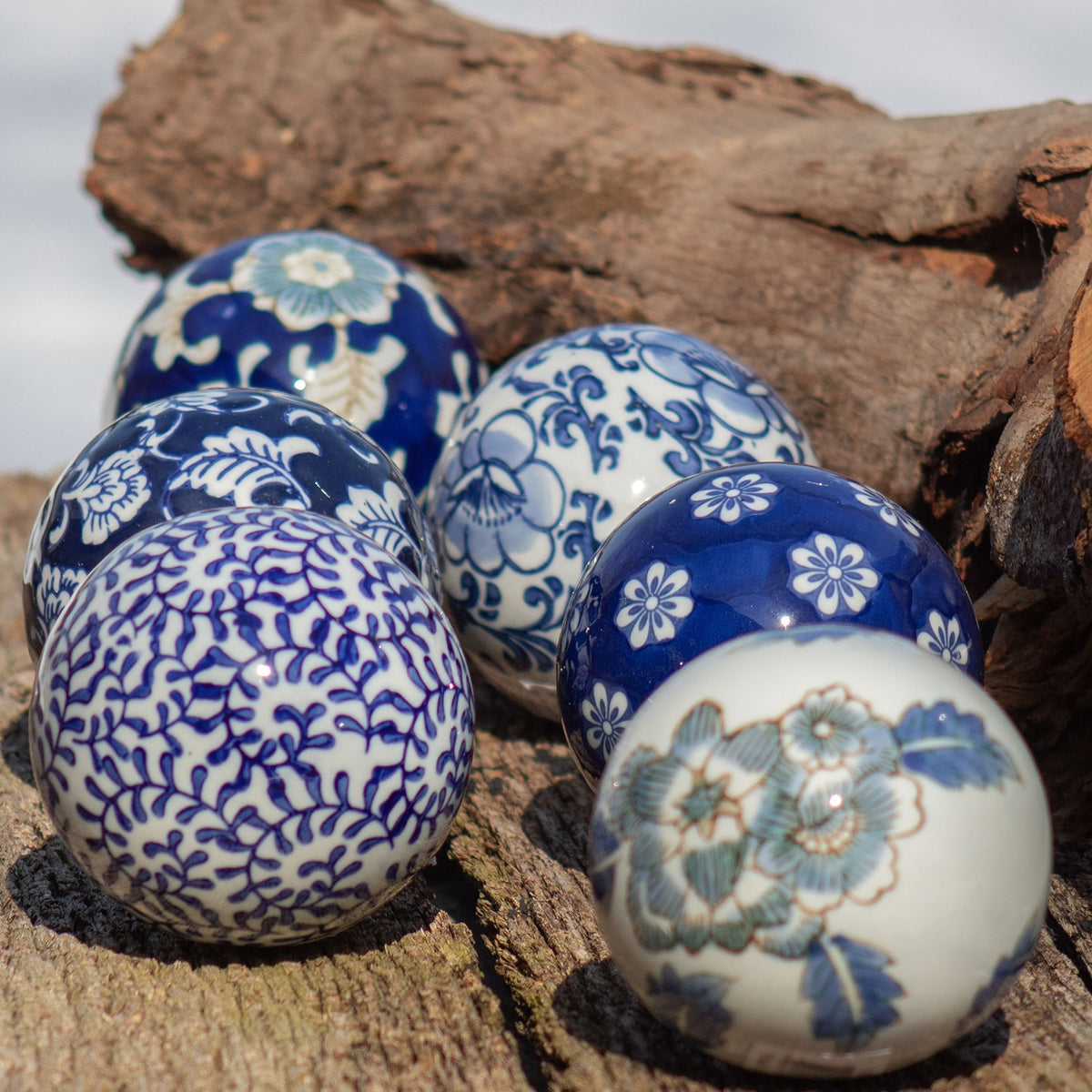 Six ceramic balls in varied blue floral patterns resting on rough wood and bark.