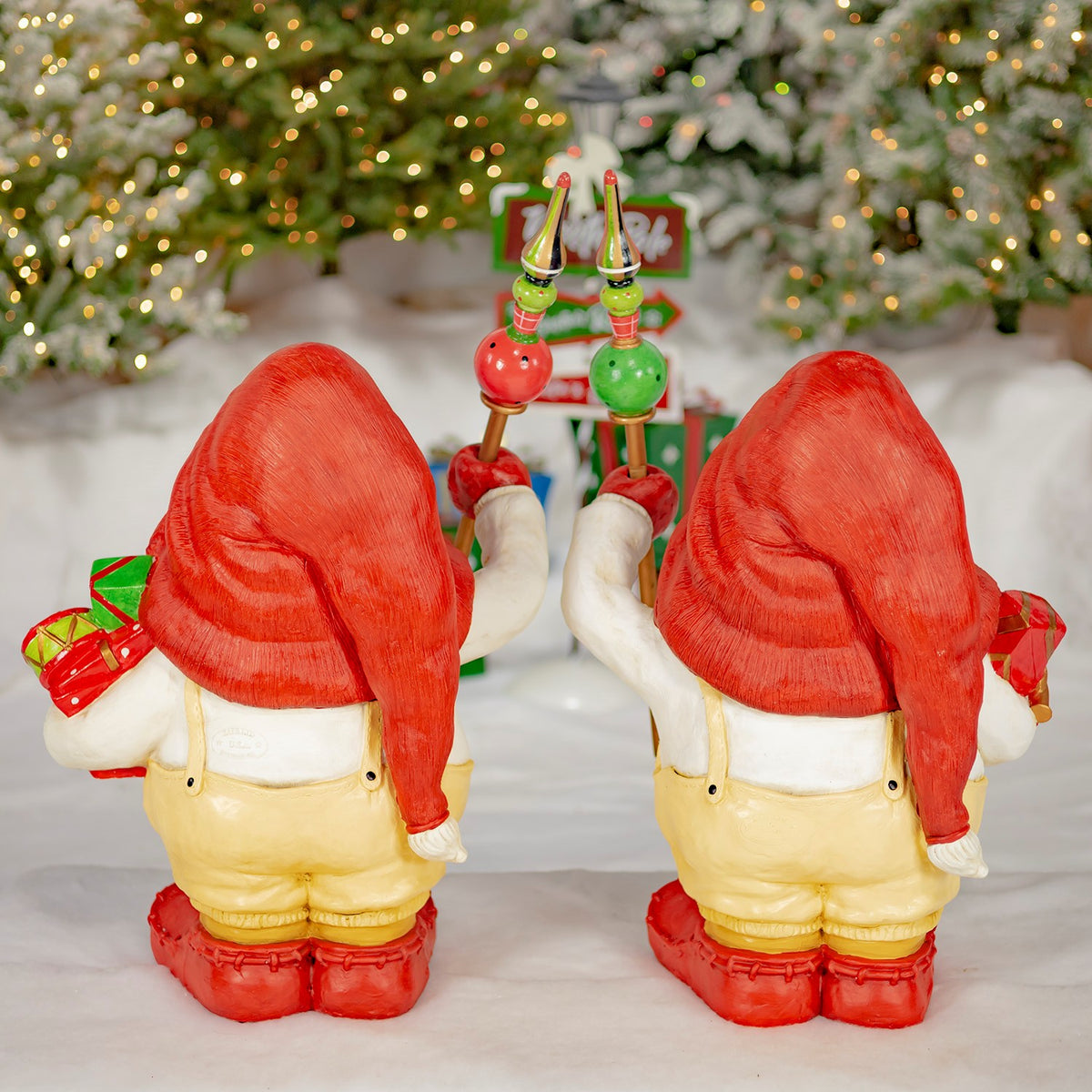 Back view of two red-hatted gnome figures holding staffs and gifts.