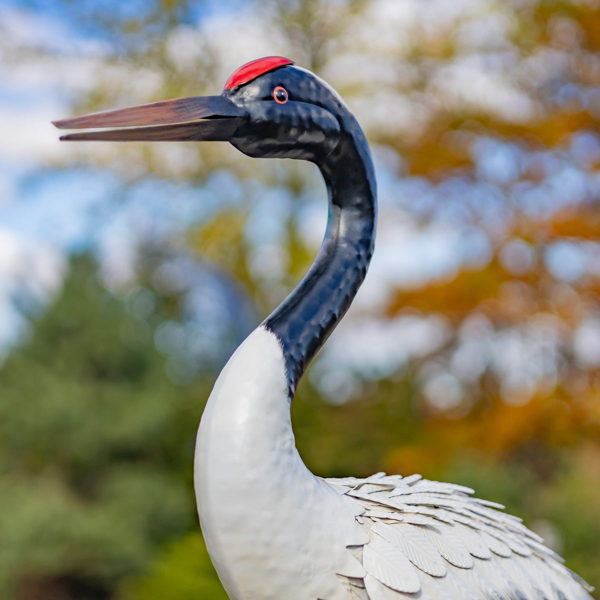 Close-up of a crane figurine’s head, curved neck, and layered white body feathers outdoors.