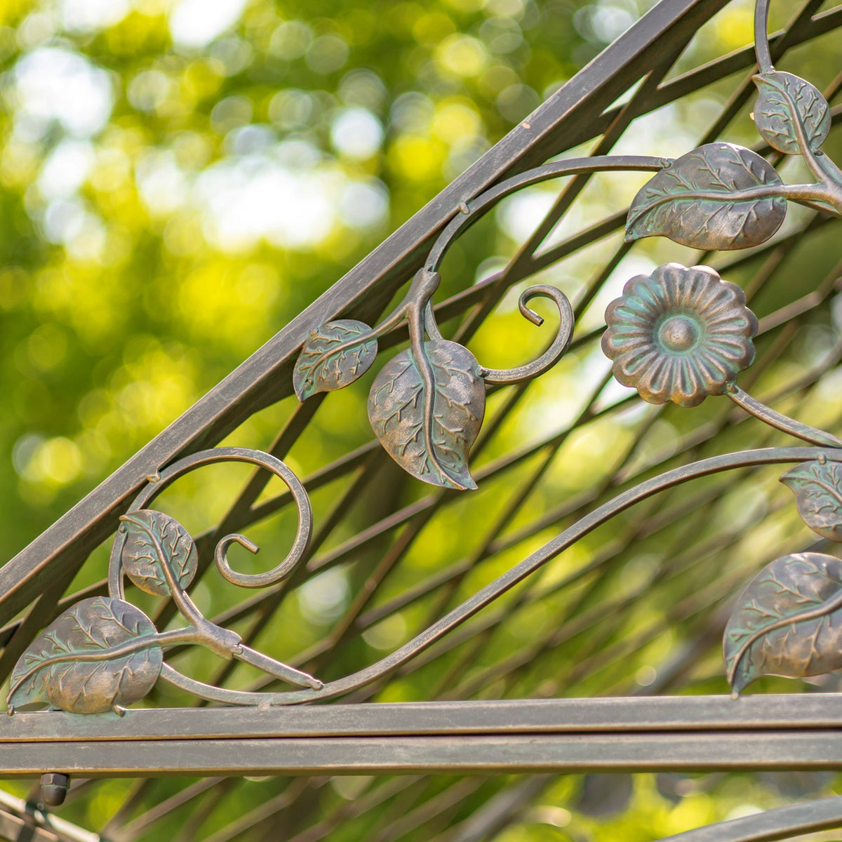 Close-up of an iron garden arch's metal flower, leaf, and curling vine ornamentation.