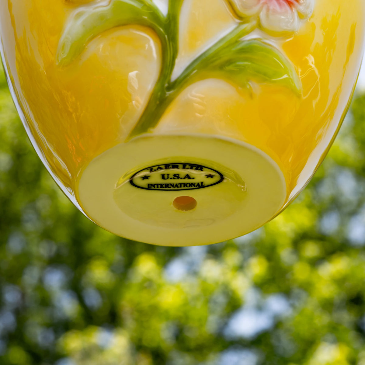 Underside of the birdhouse showing its yellow floral surface and a maker's mark.
