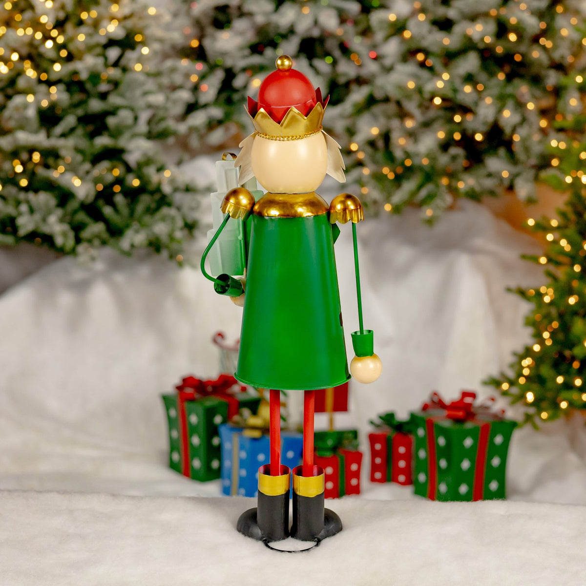 Green-coated nutcracker figurine with a red hat and gold crown, shown against a snowy holiday display.
