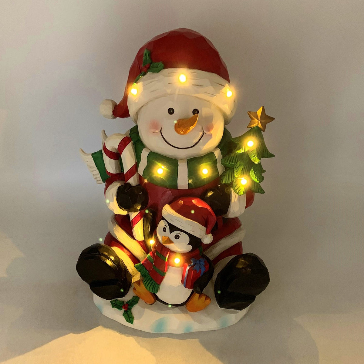 The snowman and penguin decoration glows with warm lights across the figures and tree.