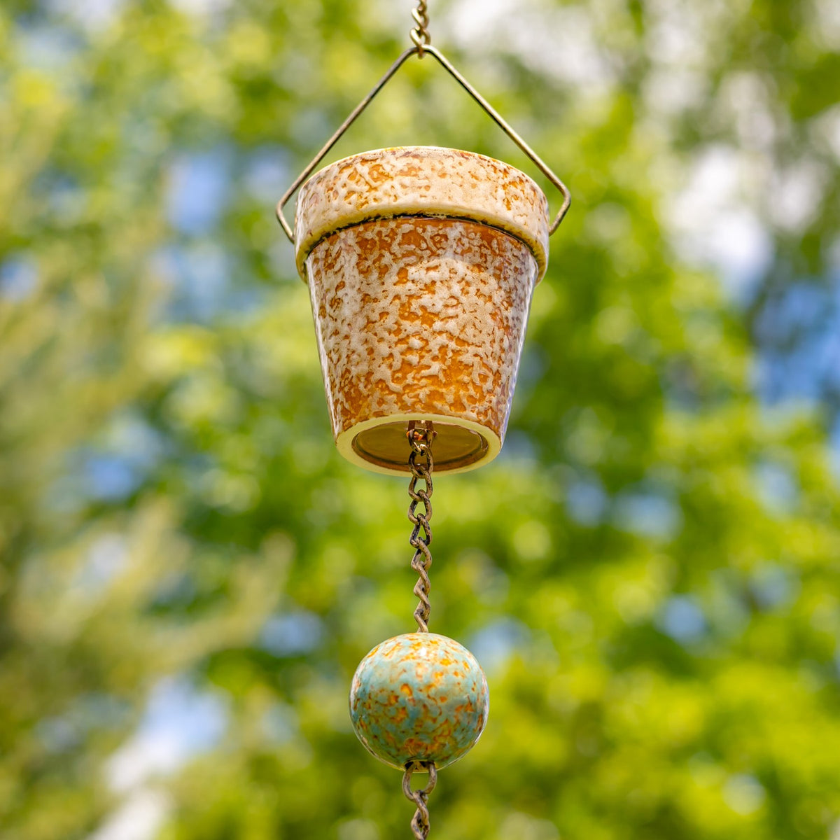 Close-up of a speckled cream-and-orange bucket, its wire handle and chain connector visible against the sky.