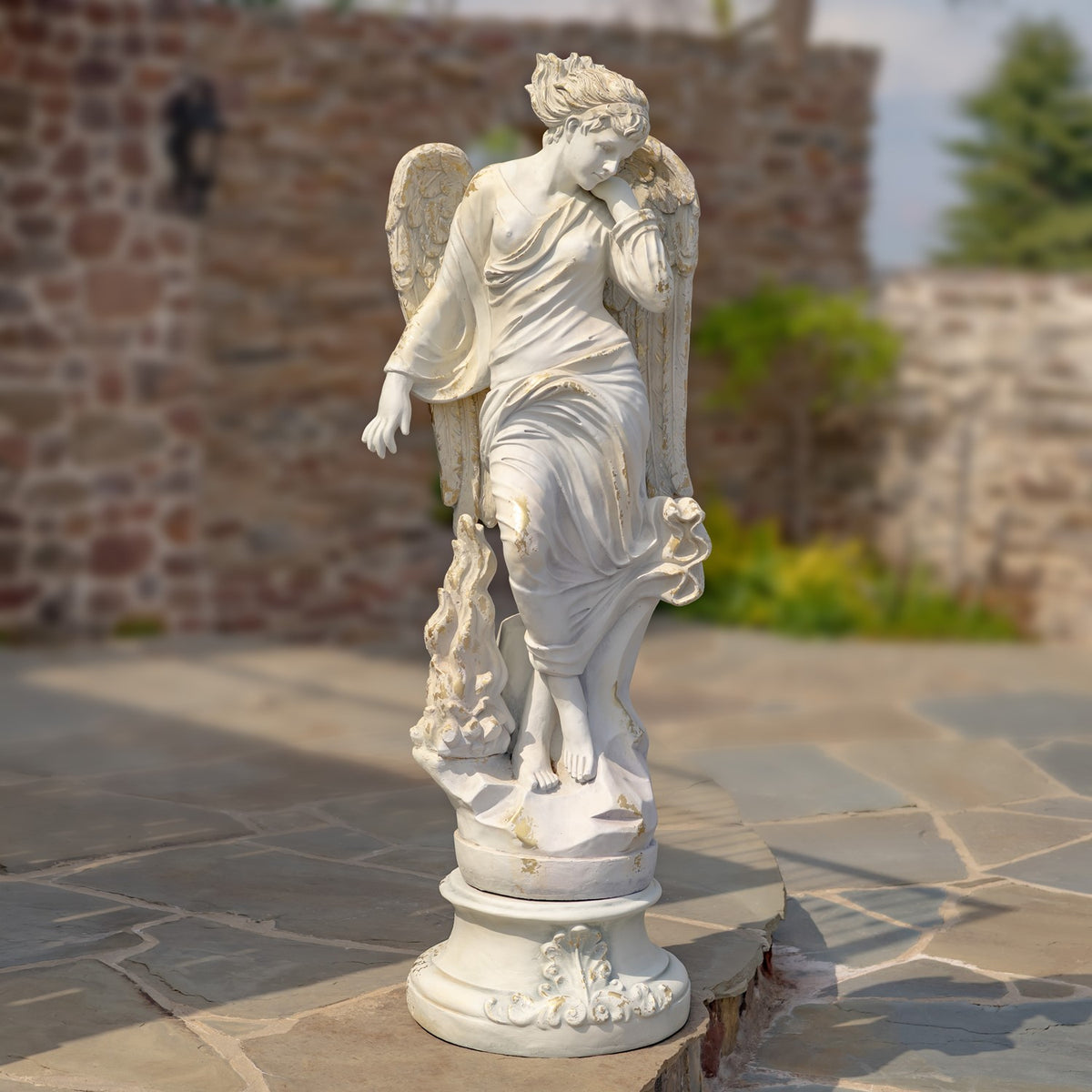 Full view of a winged angel in a flowing robe standing on a round sculpted pedestal.
