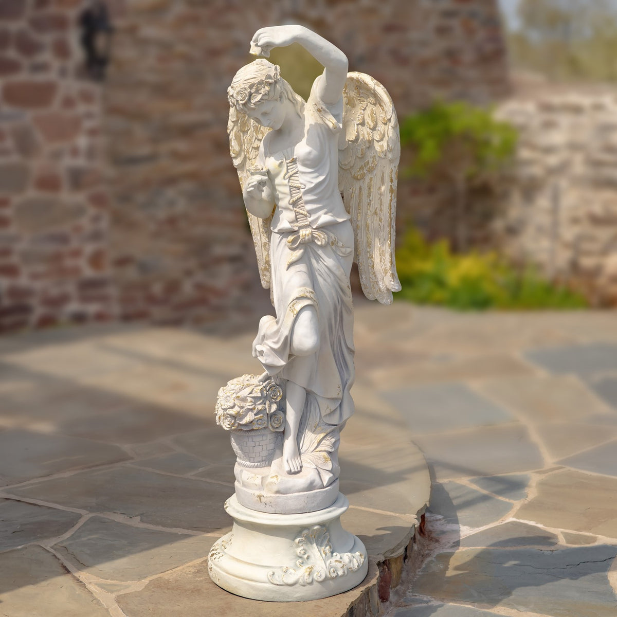 Full side view of the angel statue standing on an ornate round pedestal with a flower basket.