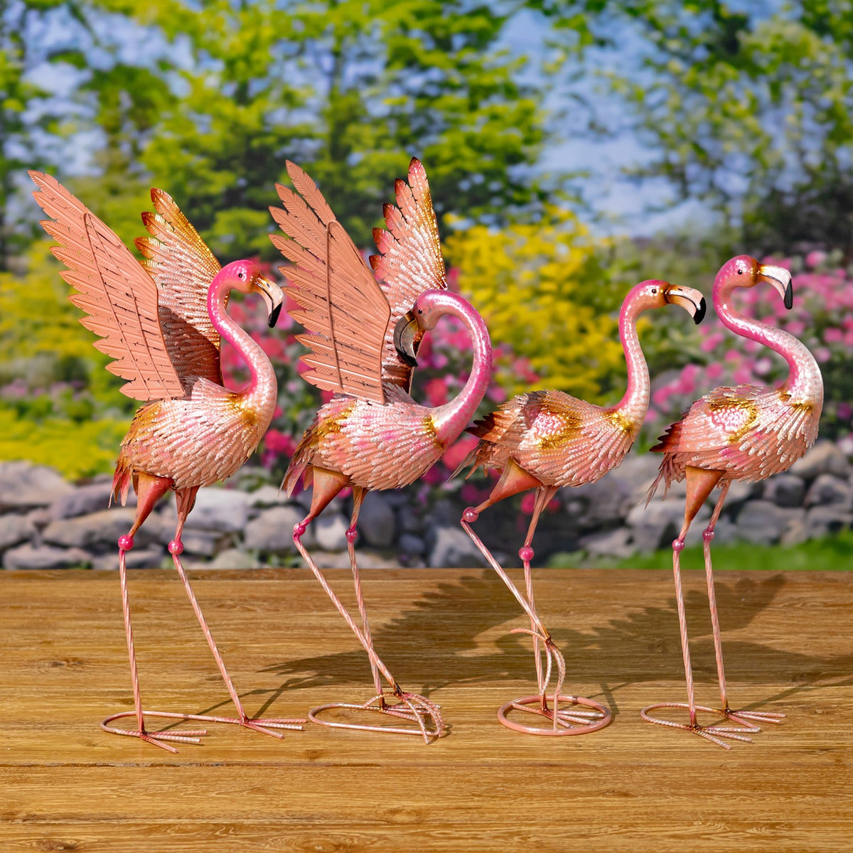 Four pink metal flamingo figurines stand together, with two displaying tall, raised wings.