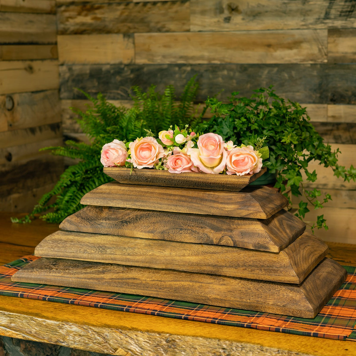 Five rectangular wooden trays stacked beneath pink roses against a leafy backdrop.
