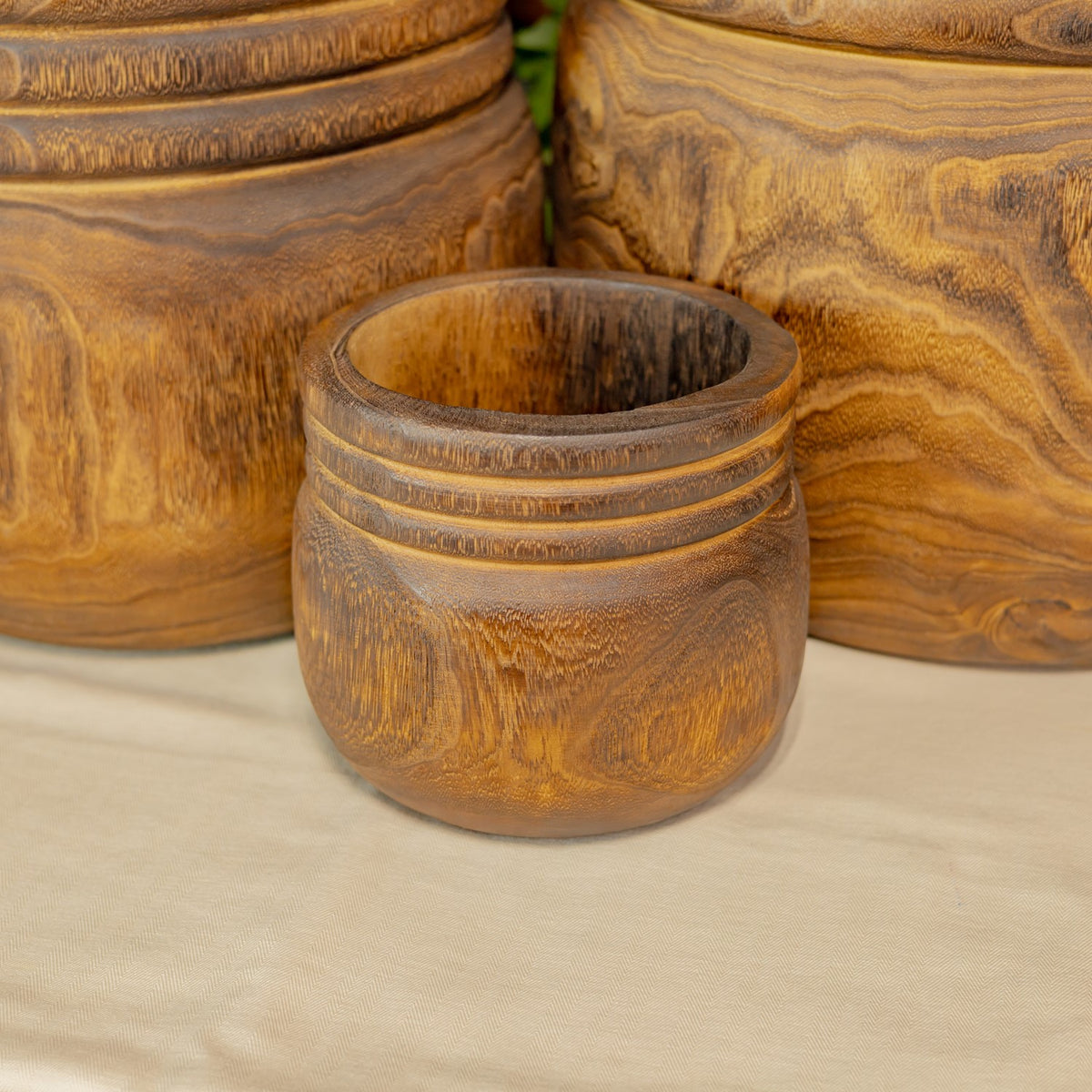 The smallest wooden bowl sits in front of two larger bowls on a light fabric surface.