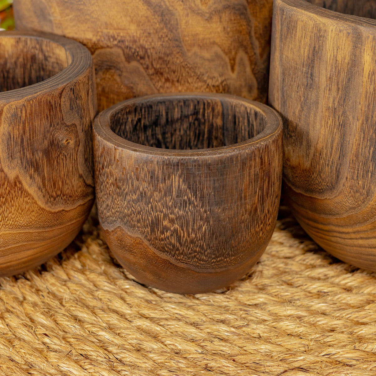 A smaller wooden bowl in front of larger bowls, resting on a textured woven mat.
