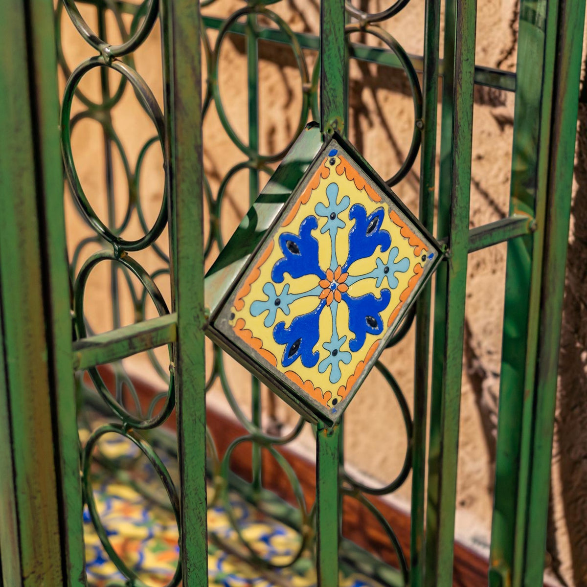Close-up of a blue, yellow, and orange patterned tile set into the green iron frame.