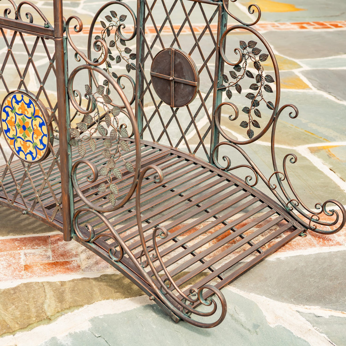 Angled view of the bridge’s slatted metal deck, lattice panels, leaf motifs, and round mosaic accents.