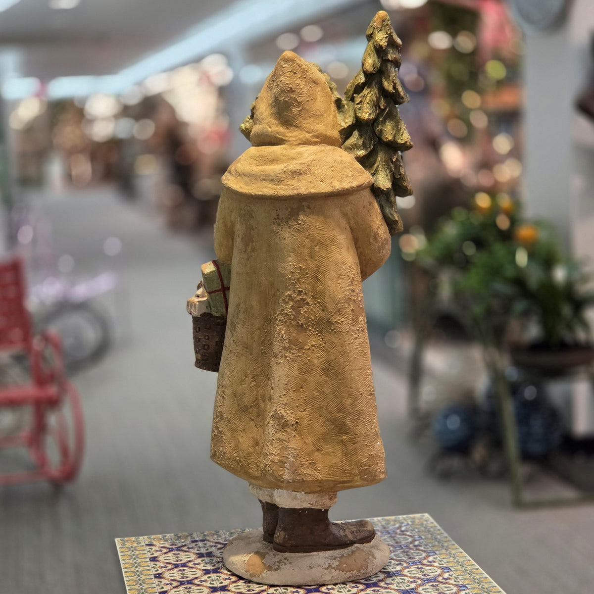Back of the Santa figurine, showing his long textured coat, boots, and the tree and basket at his sides.
