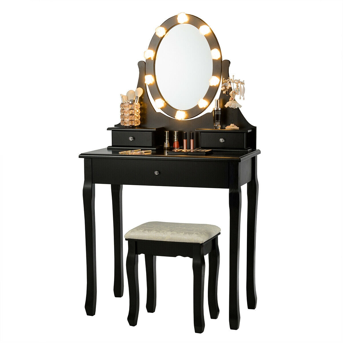 Black vanity with an oval mirror surrounded by lit bulbs, cosmetics on top, and a white-cushioned stool.