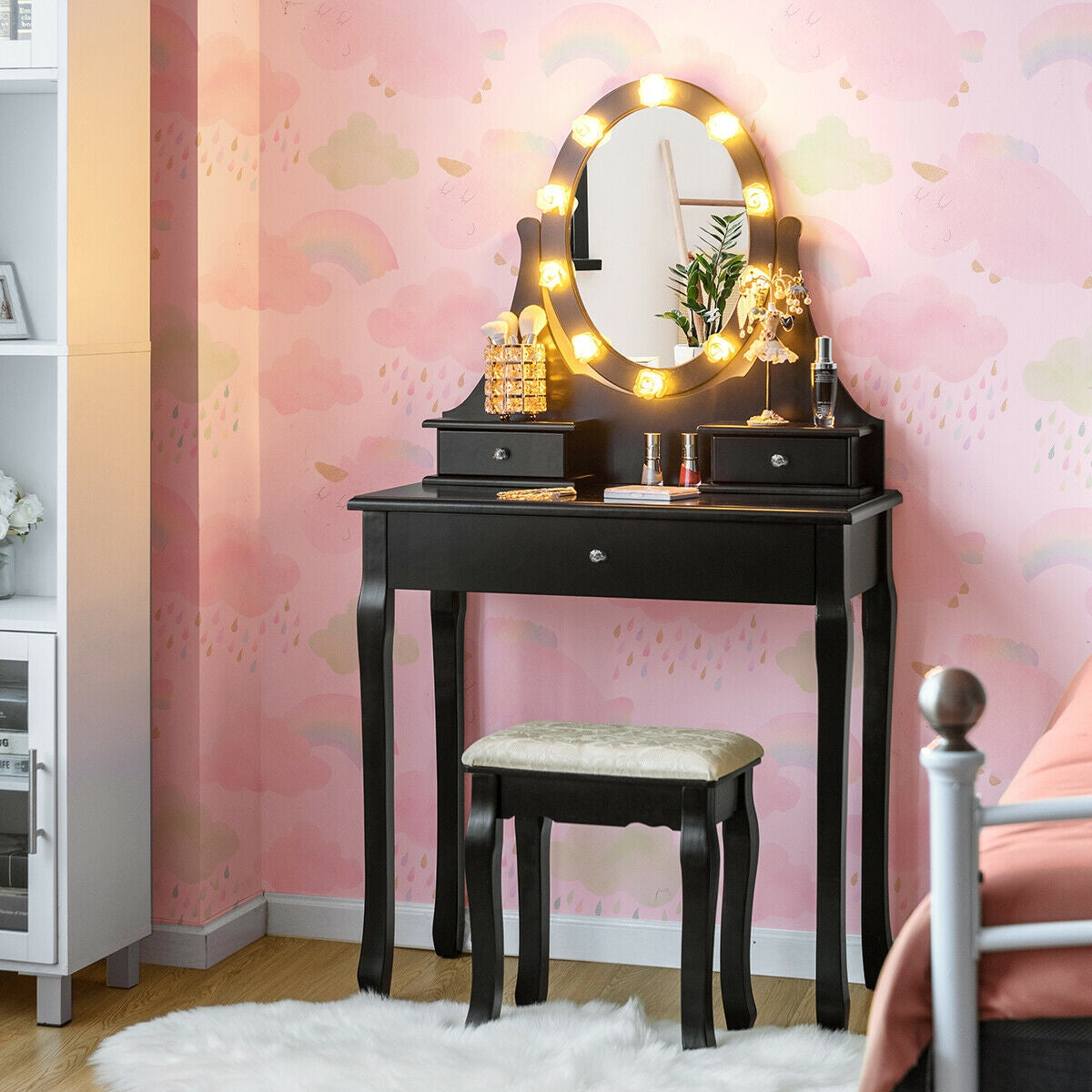 Black vanity with an oval mirror ringed by glowing bulbs and a white-cushioned stool, against pink wallpaper.